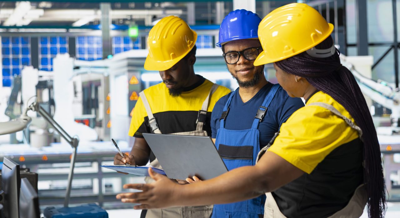 All black team of engineers comparing solar panels designs on laptop, working on the production line at the manufacturing plant. Troubleshooting and debugging to ensure optimization.